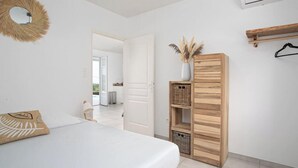 A bedroom with a bed, a wardrobe, a mirror, and a door leading to another room. - Villa Kaliemma - Tropical Villa in Martinique (Le Marin)
