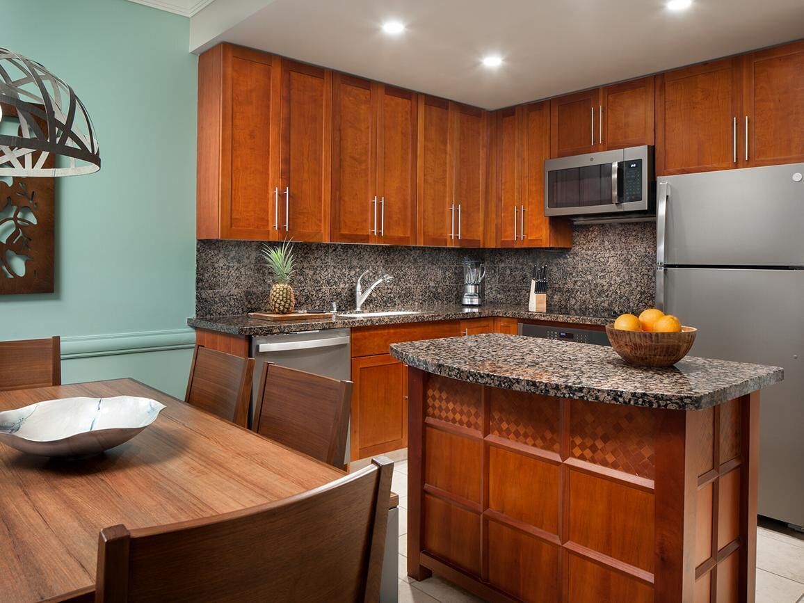 A kitchen with wooden cabinets, granite countertops, a microwave, and a refrigerator.