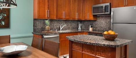A kitchen with wooden cabinets, granite countertops, a microwave, and a refrigerator.