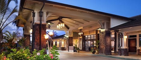 A hotel entrance with a covered walkway, palm trees, and a well-lit facade.