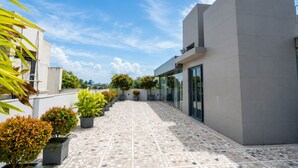 A modern building with a tiled patio, potted plants, and a clear sky. - The Bay Suites - Salt Lake AE Market (Bidhannagar)