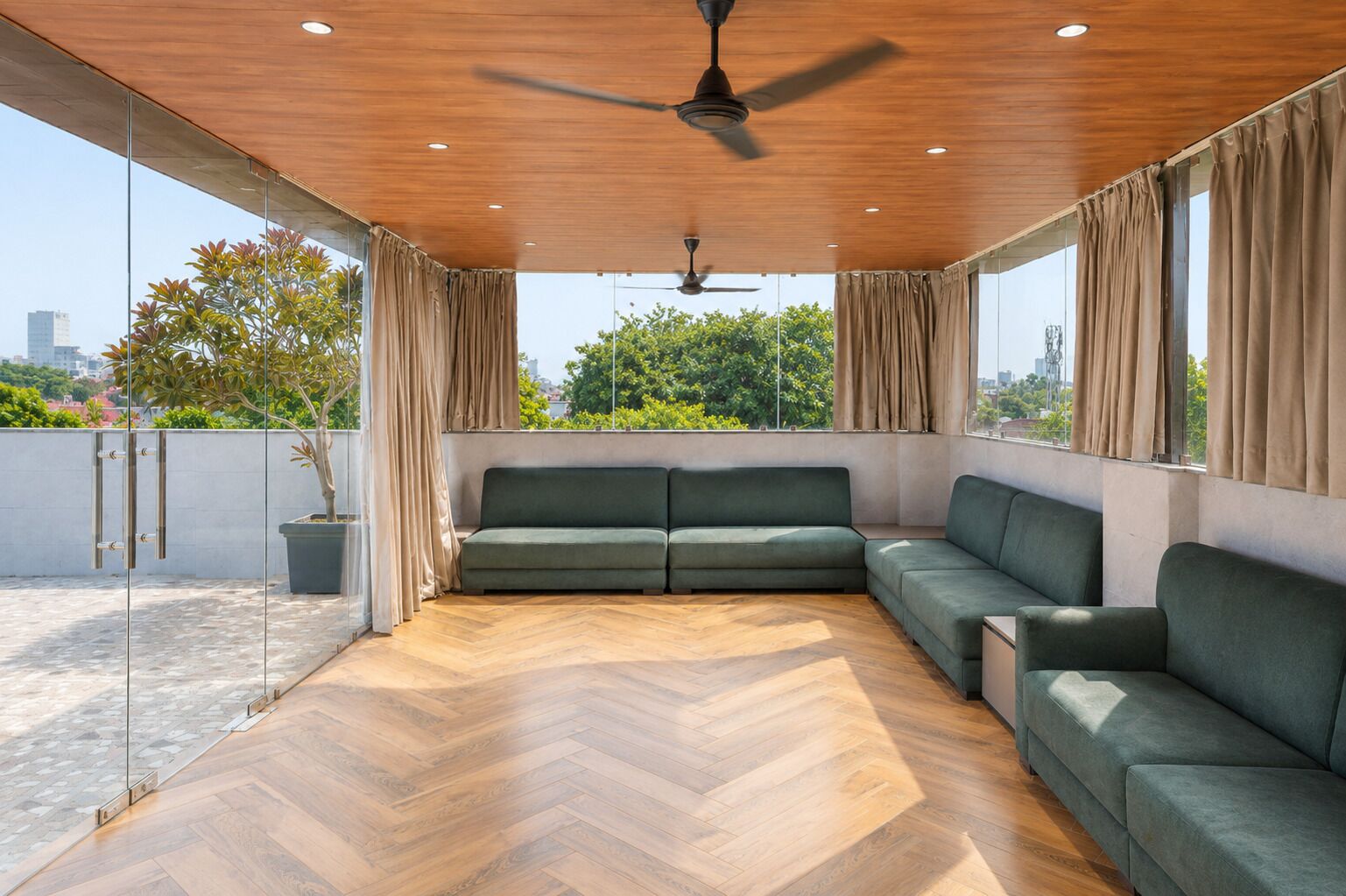 Un salón moderno con suelo de madera en espiga, un sofá modular, un ventilador de techo y ventanas grandes con cortinas.