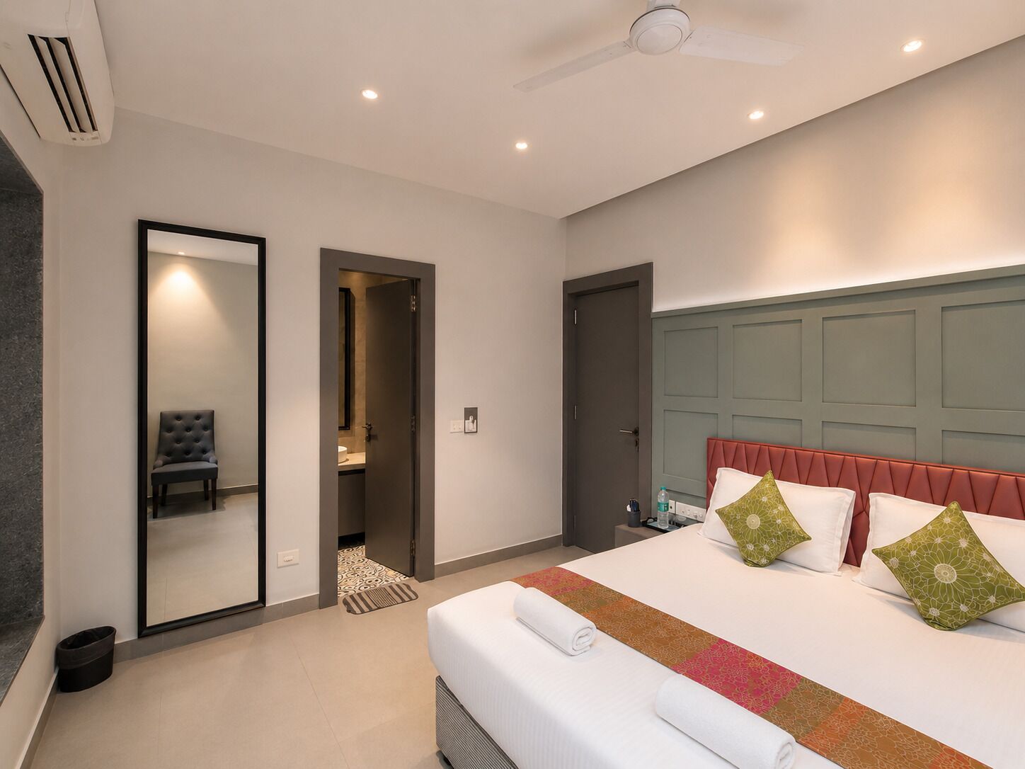 A hotel room with a bed, a chair, a door, and a ceiling fan.