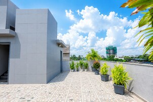 A rooftop terrace with potted plants, a tiled floor, and a view of the city skyline.