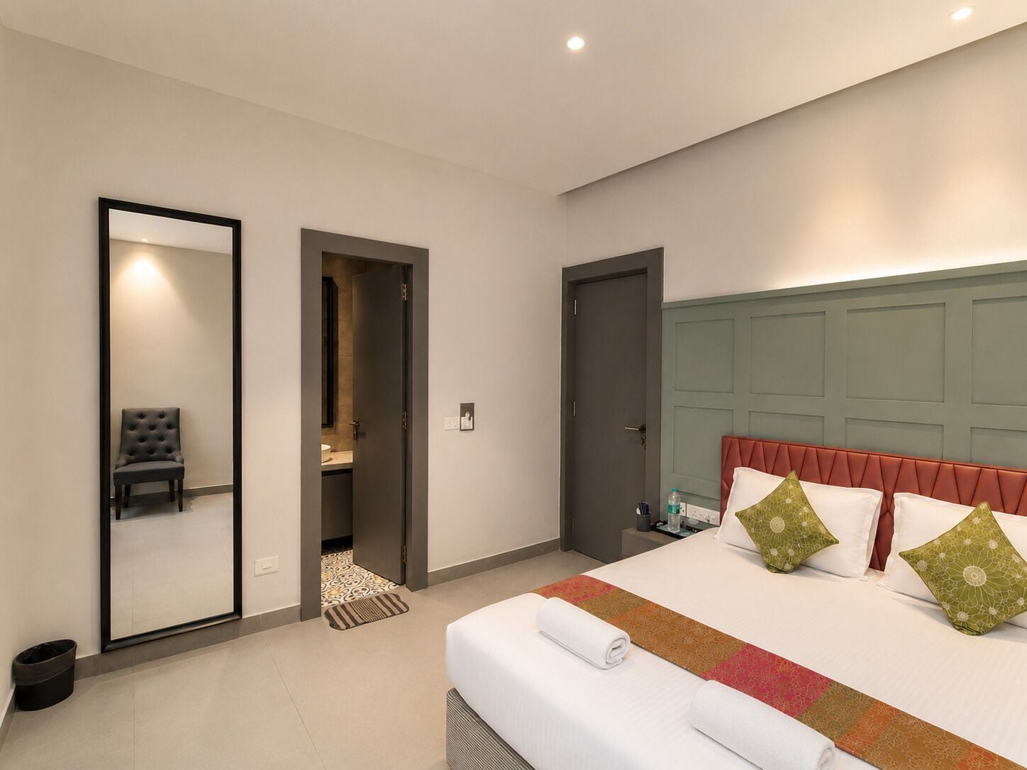 Une chambre d’hôtel moderne, dotée d’un grand lit, d’un miroir, d’une chaise et d’une porte donnant accès à la salle de bain.