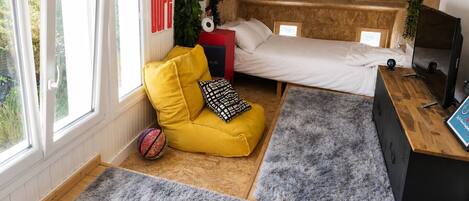 A bedroom with a bed, a yellow sofa, a grey rug, and a TV.
