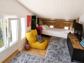 Un dormitorio con una cama, un sofá amarillo, un tapete gris y un televisor.