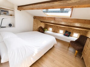 Ein Schlafzimmer mit einem großen Bett, einer hölzernen Bank mit Kissen, einem Sessel und einem Dachfenster.