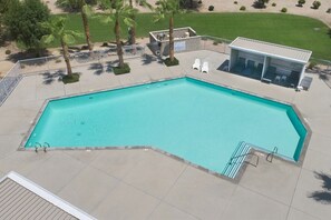 A rectangular swimming pool with a tiled deck, surrounded by a metal fence, palm trees, and a small building with a roof. - Chic Indian Wells Pool, 4 BD-Next to Tennis Garden (Indian Wells)