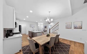 A modern kitchen with white cabinetry, a dining area with a wooden table and chairs, and a staircase leading to another level. - Millville by the Sea- shuttle access Bethany beach (Millville)