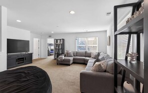 A modern living room with a sectional sofa, a flat-screen TV, and a large mirror. - Millville by the Sea- shuttle access Bethany beach (Millville)