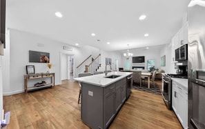 A modern kitchen with a central island, built-in appliances, and a dining area with a staircase. - Millville by the Sea- shuttle access Bethany beach (Millville)