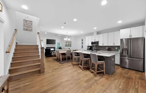 A modern kitchen with a central island, stainless steel appliances, and a dining area with a wooden table and chairs. - Millville by the Sea- shuttle access Bethany beach (Millville)