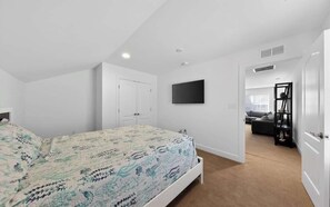 Una camera da letto con un letto, una TV fissata al muro e una porta che dà su un'altra stanza.