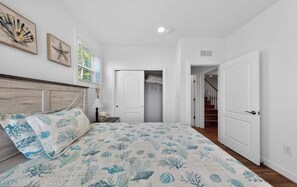 A bedroom with a bed, a nightstand, a lamp, a closet, and a staircase leading to another floor. - Millville by the Sea- shuttle access Bethany beach (Millville)