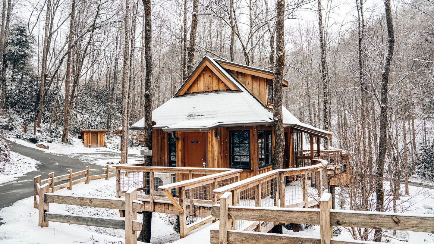 A wooden cabin with a balcony, surrounded by a snowy forest.