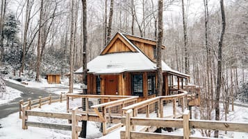 A wooden cabin with a balcony, surrounded by a snowy forest.