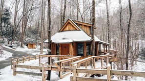 Une cabane en bois dotée d’un balcon, entourée d’une forêt enneigée.