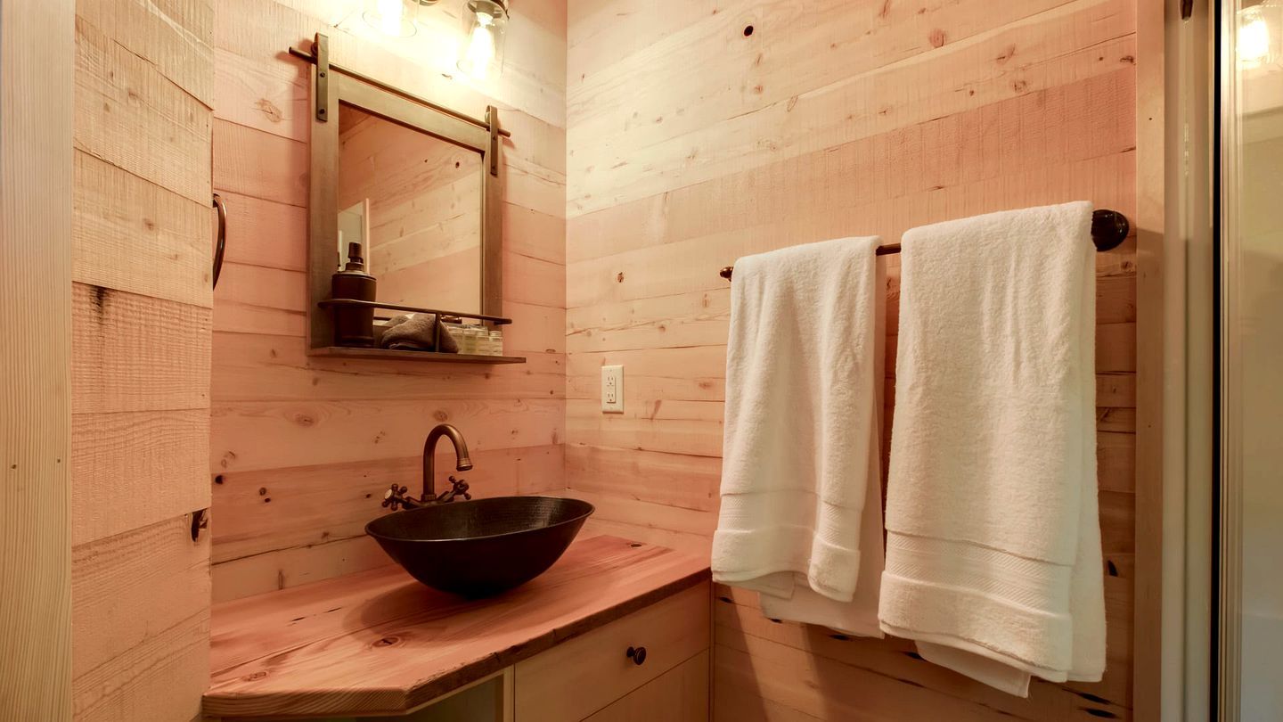 A wooden cabin bathroom with a wooden sink, a mirror, and two towels hanging on a rack.
