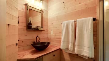 Baño de cabaña de madera con lavamanos de madera, un espejo y dos toallas colgadas en un perchero.
