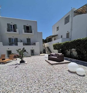 Ein modernes Gebäude mit weißer Fassade, einem Außenbereich mit einer Couch und Sesseln sowie einem Kieshof.