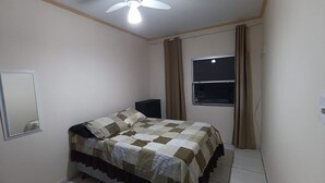 Een slaapkamer met een bed, een plafondventilator, een raam met gordijnen en een spiegel aan de muur.
