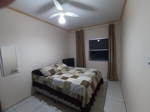 Ein Schlafzimmer mit Bett, Deckenventilator, einem Fenster mit Vorhängen und einem an der Wand befestigten Spiegel.