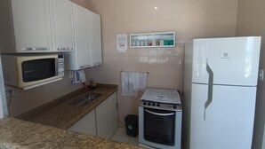 Een kleine keuken met witte kastjes, een magnetron, een oven en een koelkast.