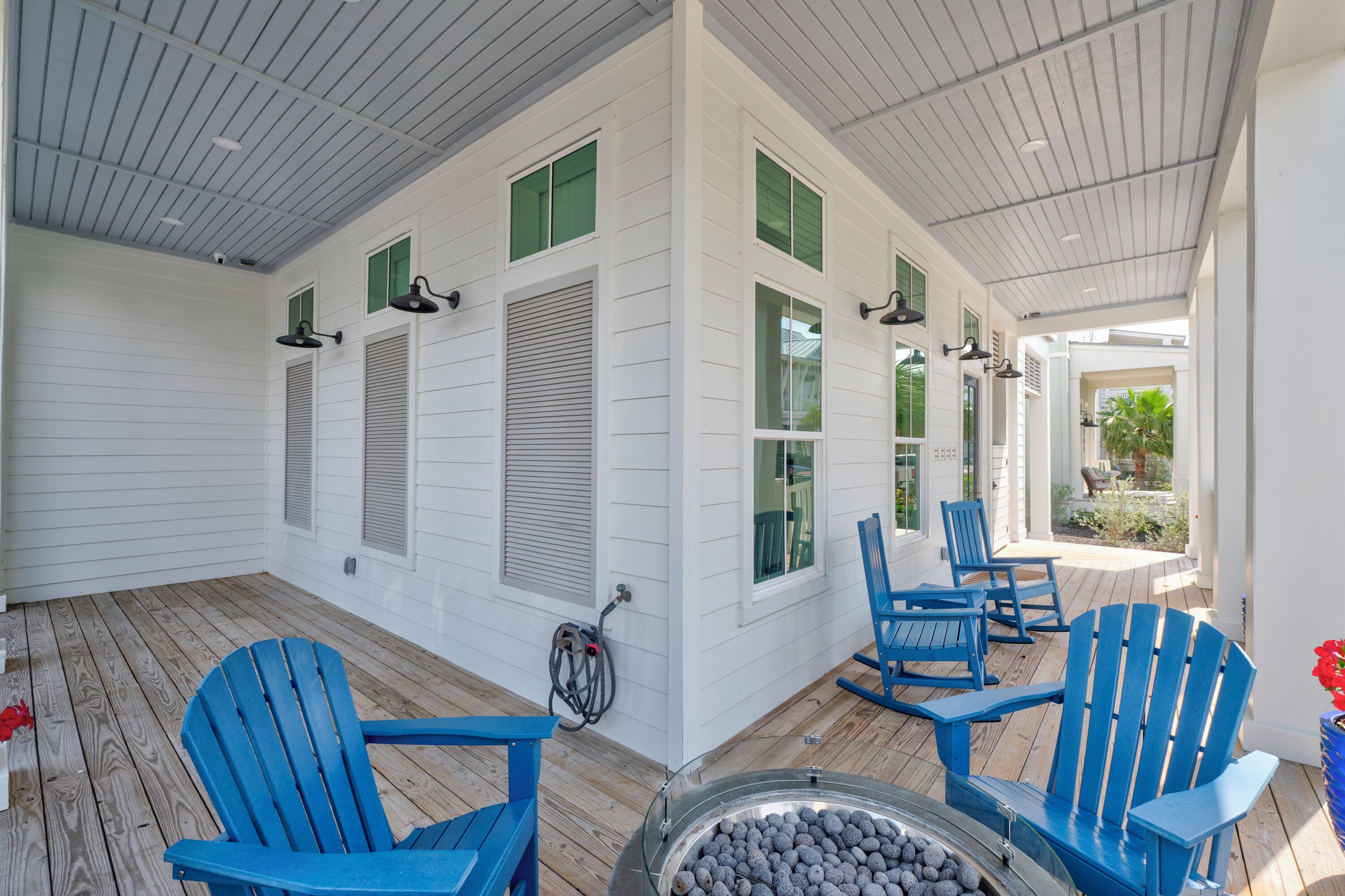 A covered porch with white siding, green windows, and blue Adirondack chairs.