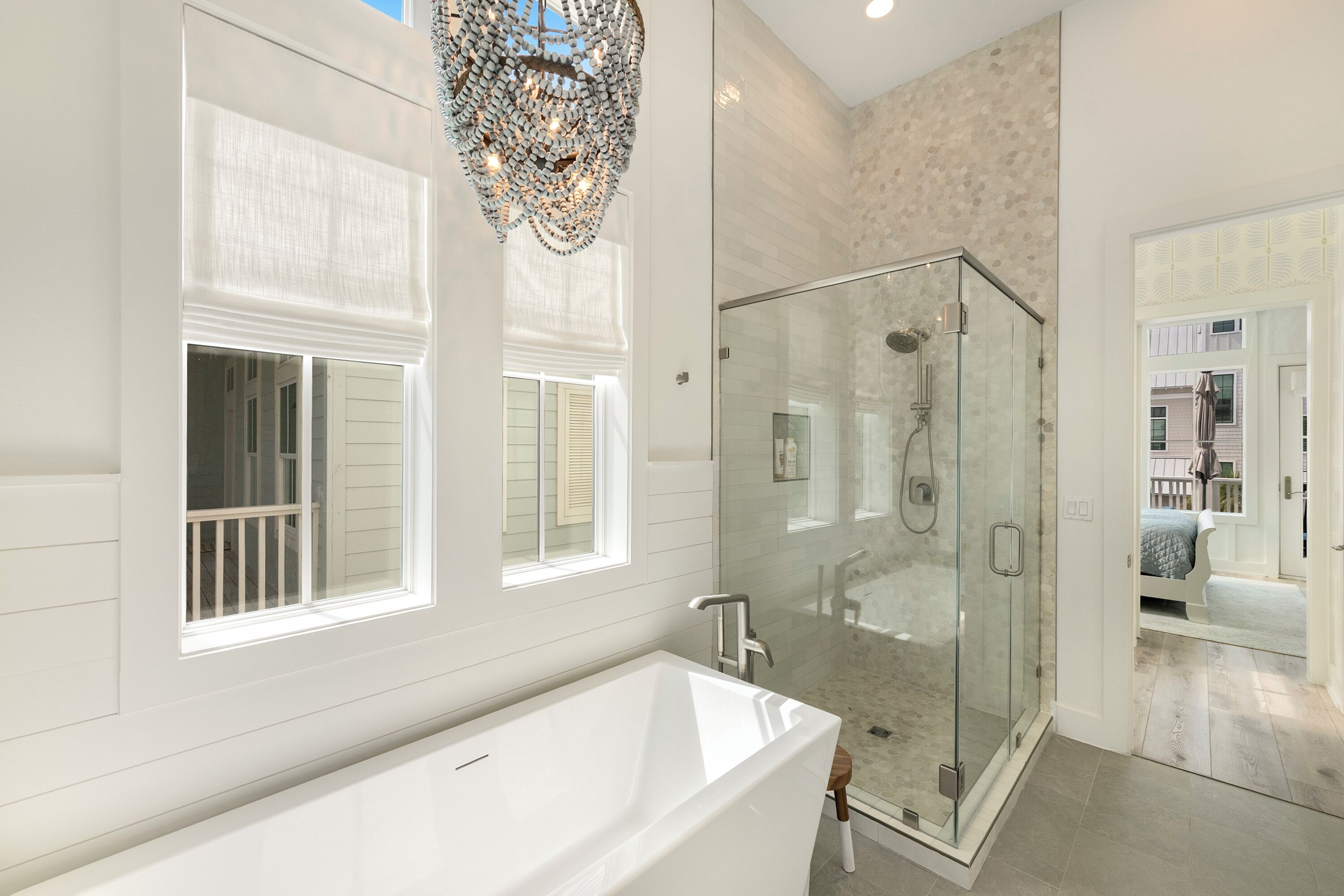 A modern bathroom with a glass-enclosed shower, a freestanding bathtub, and a decorative chandelier.