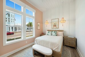 Ein Schlafzimmer mit großem Fenster, einem Bett mit Steppdecke, zwei Nachttischen und einer Bank.