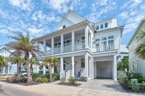 A two-story house with a covered porch, a garage, and a well-maintained garden with palm trees. - Seas & Sunsets 201 LAK (Port Aransas)