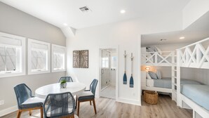 A modern interior with a round dining table, blue chairs, a white sofa, and a loft bed with a ladder. - Seas & Sunsets 201 LAK (Port Aransas)