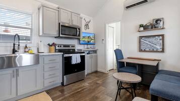 A modern kitchen with stainless steel appliances, a dining area with a blue chair, and a small round table.