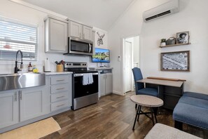 A modern kitchen with stainless steel appliances, a dining area with a blue chair, and a small round table. - Comfortable Tiny Home Retreat with Resort Amenities Near Fredericksburg, TX (Fredericksburg)
