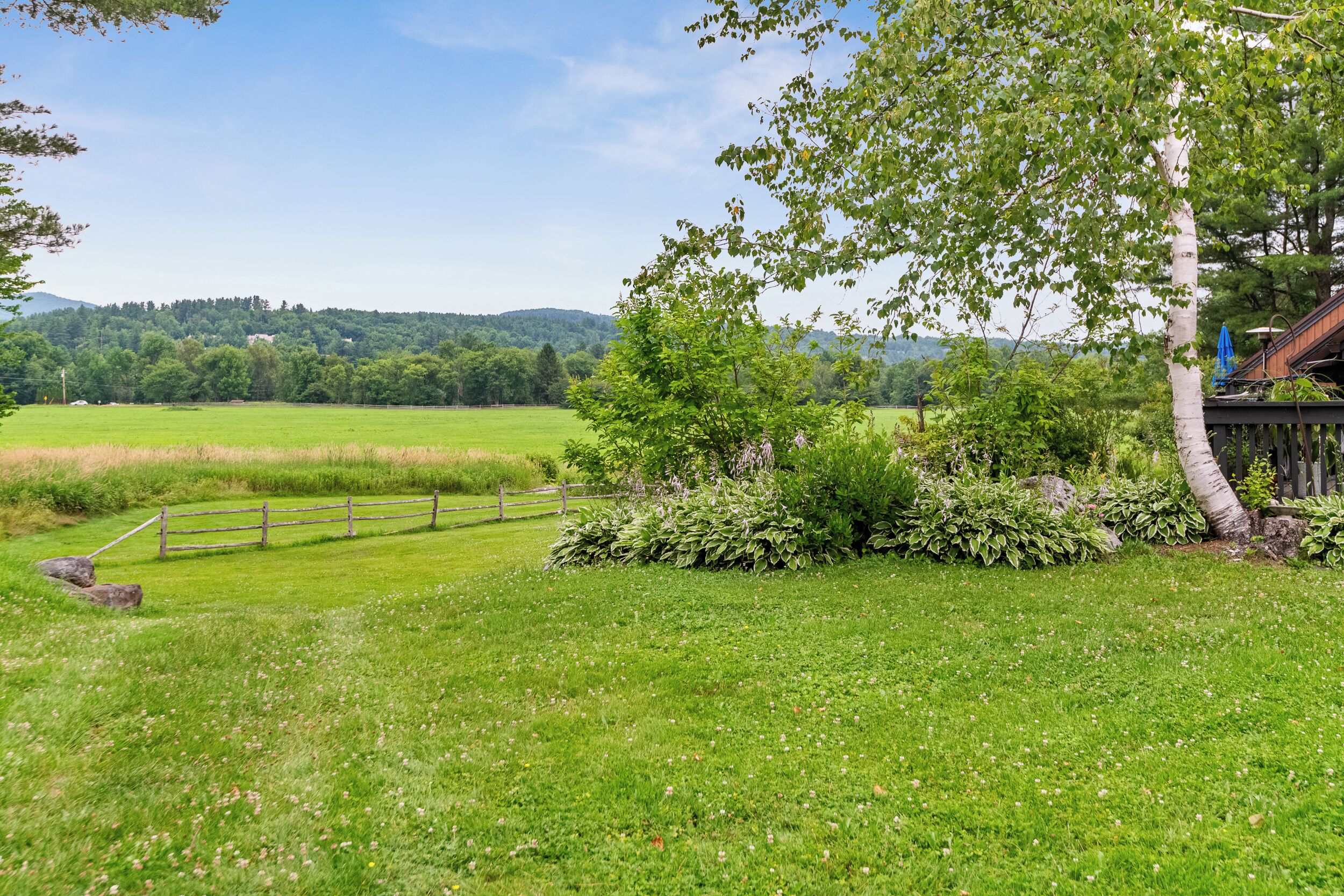 A rural landscape with a wooden fence, a small pond, and a house with a blue roof.
