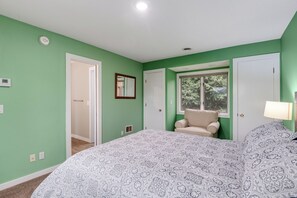 A bedroom with green walls, a bed with patterned bedding, a window with a view, and a door leading to another room.