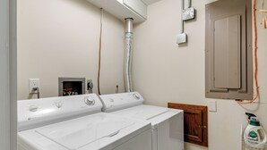 Une buanderie équipée de deux machines à laver et deux sèche-linge superposés, d’un chauffe-eau et d’un meuble de rangement.