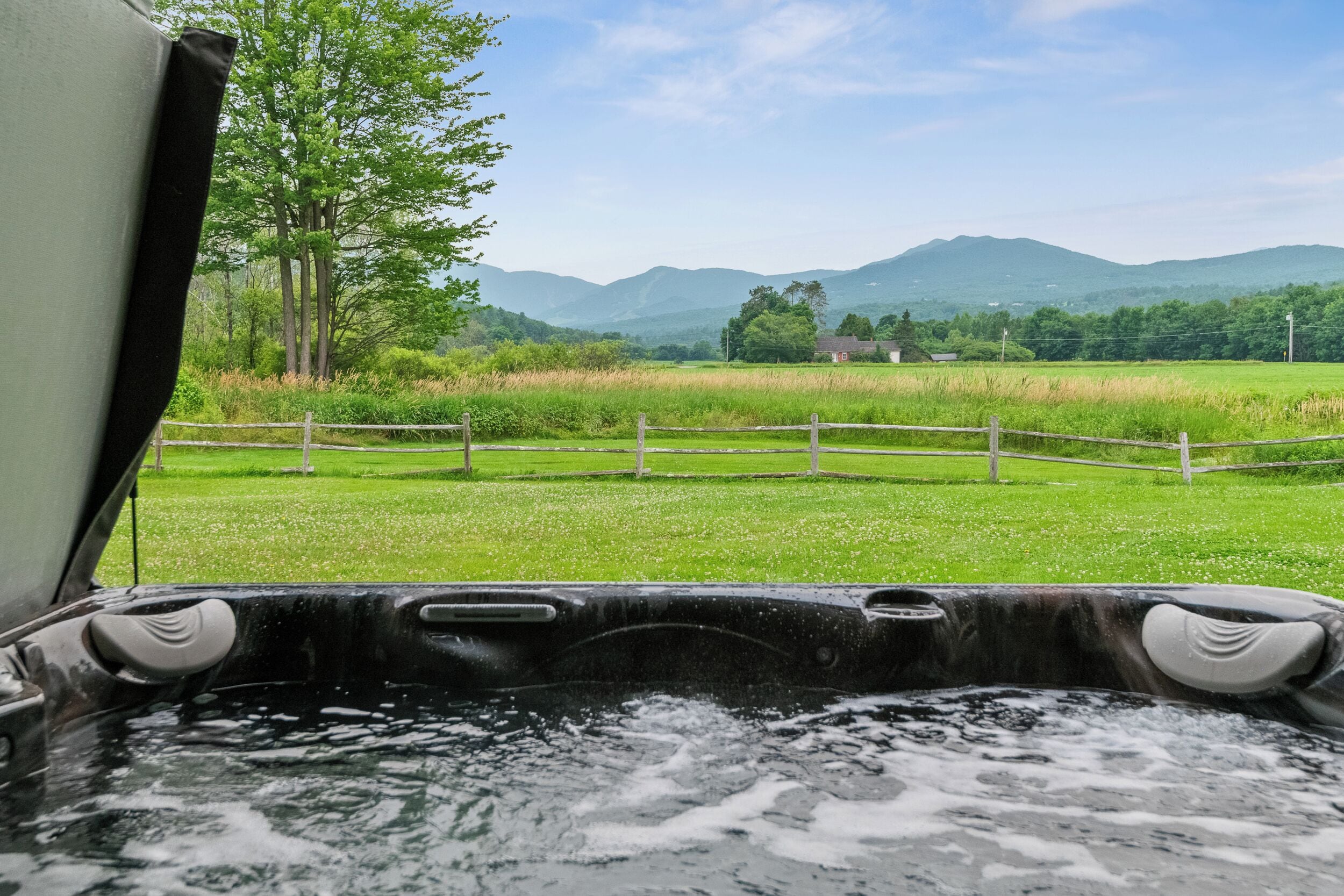 A hot tub with a view of a green field and mountains in the background.