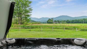 A hot tub with a view of a green field and mountains in the background.