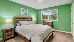 Une chambre à coucher avec un lit, deux tables de chevet, une fenêtre et un tableau accroché au mur.