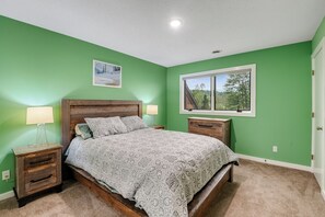 Quarto com cama, duas mesas de cabeceira, uma janela e um quadro pendurado na parede.