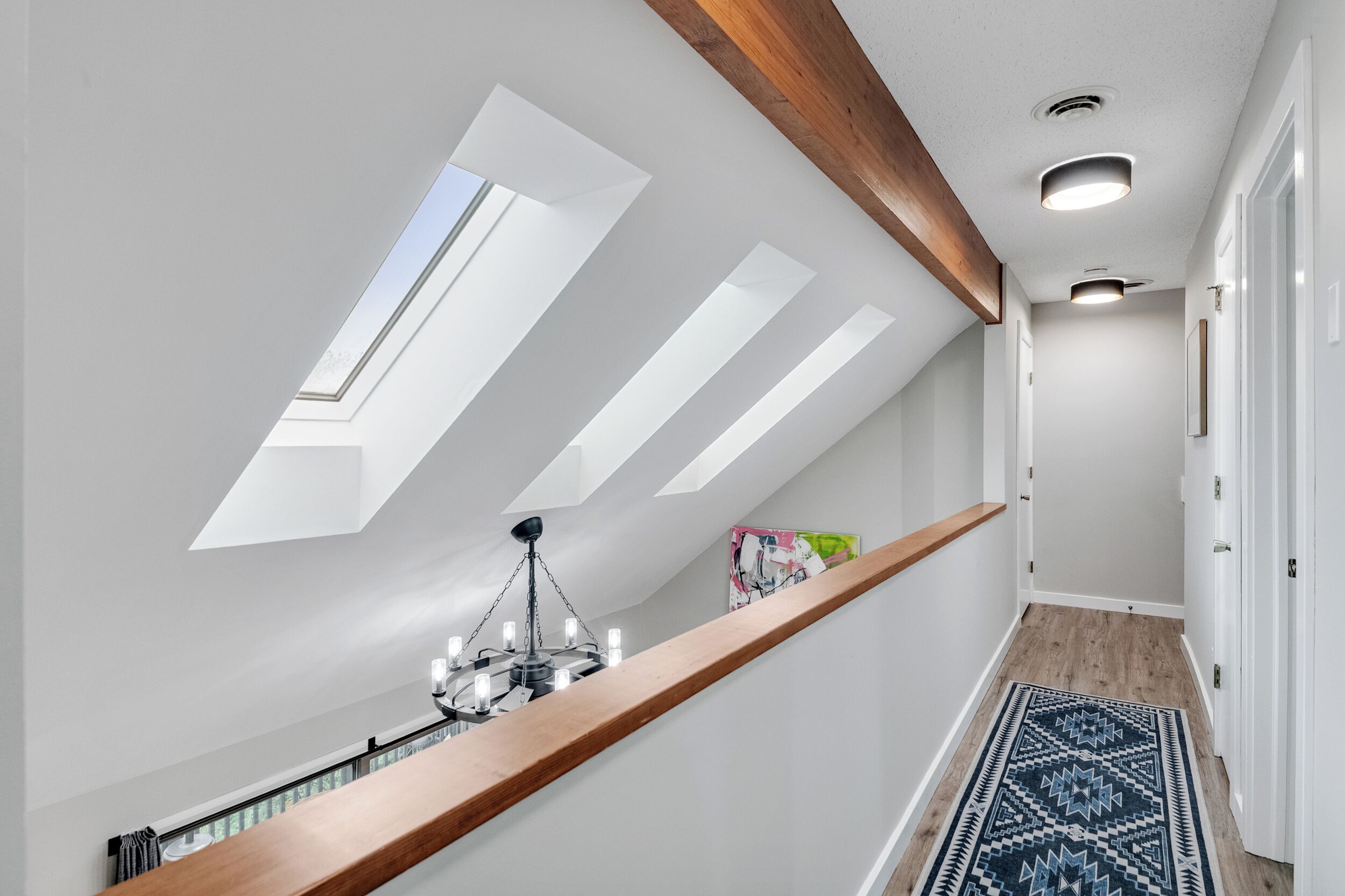 Ein modernes Interieur mit Dachfenstern, Holzbalkendecke, einer Chandelierleuchtre und einem gemusterten Teppich.