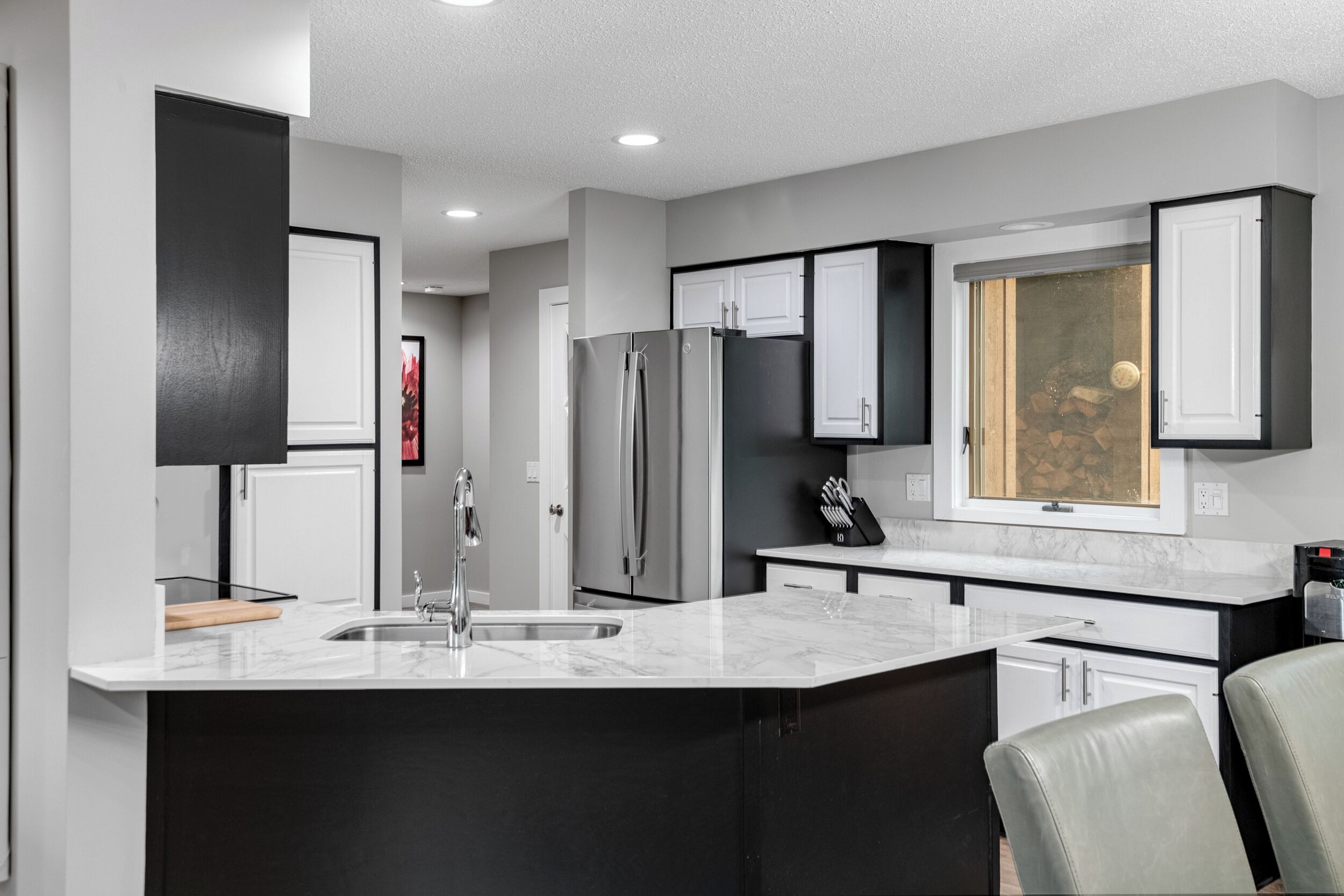 A modern kitchen with a central island, stainless steel appliances, and a window with a view of a stone wall.