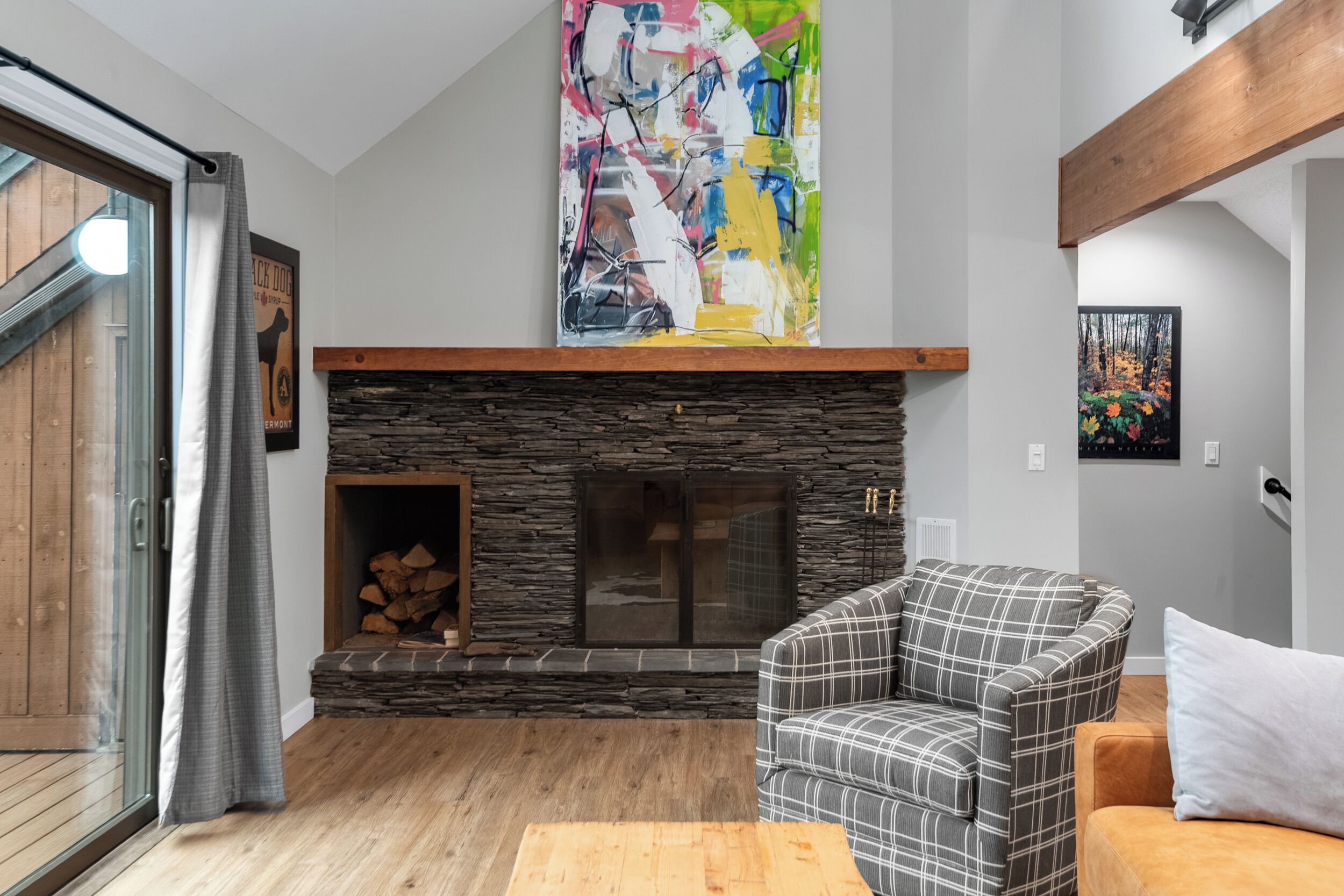 A living room with a stone fireplace, a plaid sofa, and a large abstract painting above the fireplace.