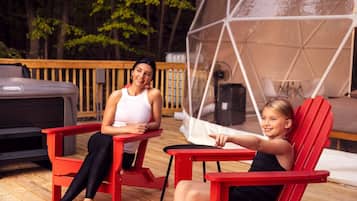 Two people seated on red chairs outdoors with a tent structure in the background.