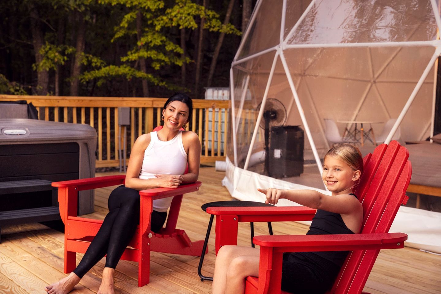 Two people seated on red chairs outdoors with a tent structure in the background.