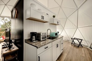 Una cocina compacta con gabinetes blancos, una encimera, un fregadero, una cafetera, un tostador y un microondas.