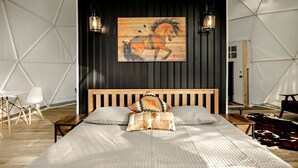 Ein Schlafzimmer mit einem hölzernen Bett, zwei Wandleuchten, einem Gemälde eines Holzpferdes und einem Kuhfellteppich.
