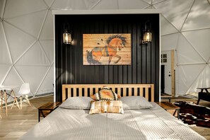 Un dormitorio con una cama de madera, dos lámparas de pared, un cuadro de un caballo de madera y una alfombra de cuero de vaca.